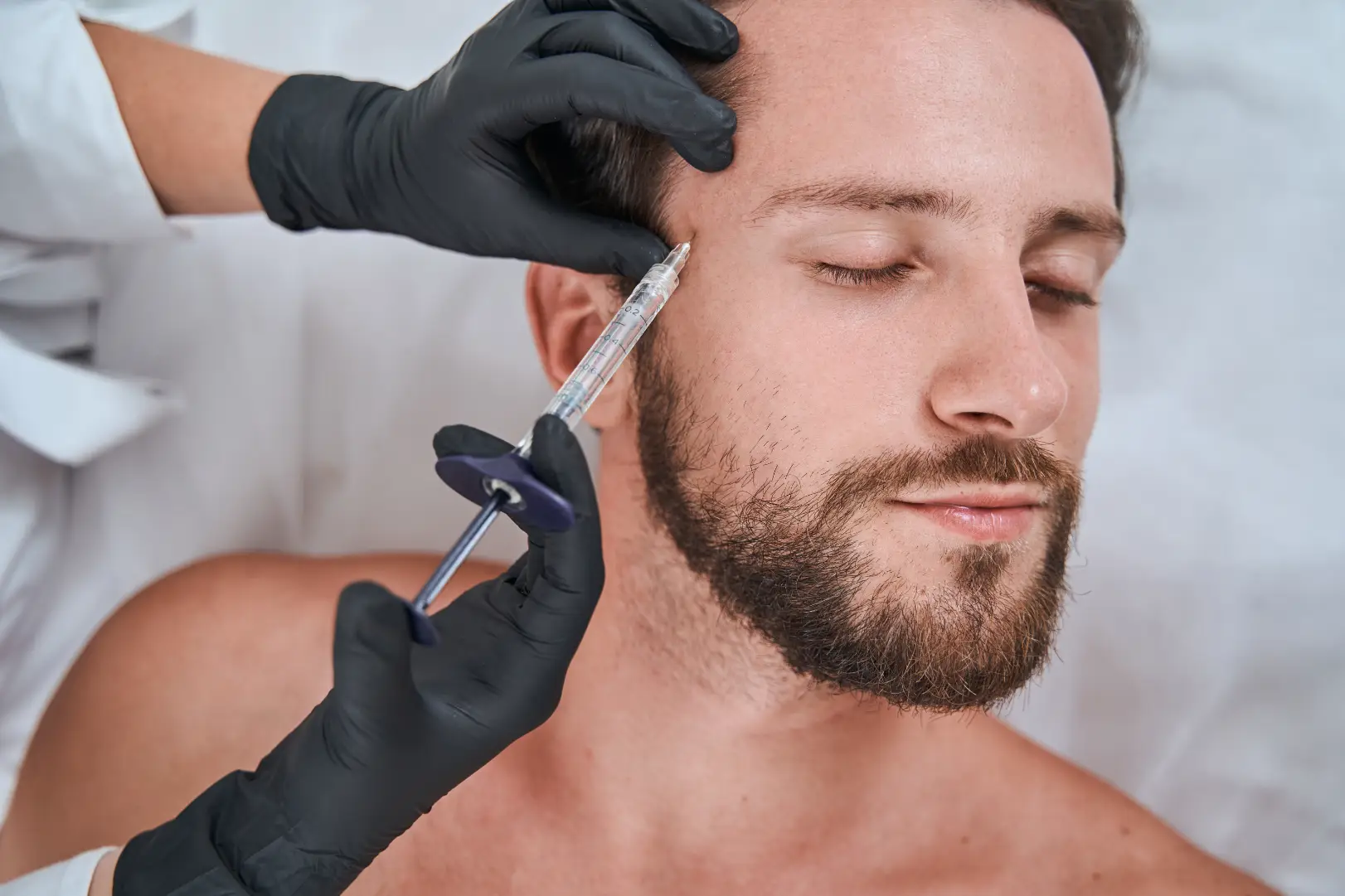 Man receiving facial injection near temple during cosmetic treatment