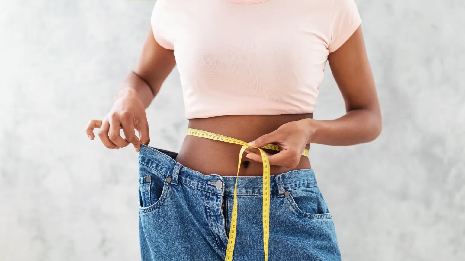 Person measuring waist with tape while holding loose-fitting jeans