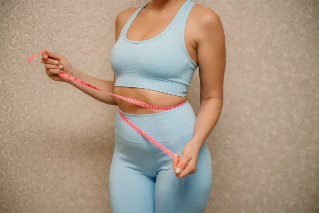 Woman measuring waist with pink measuring tape